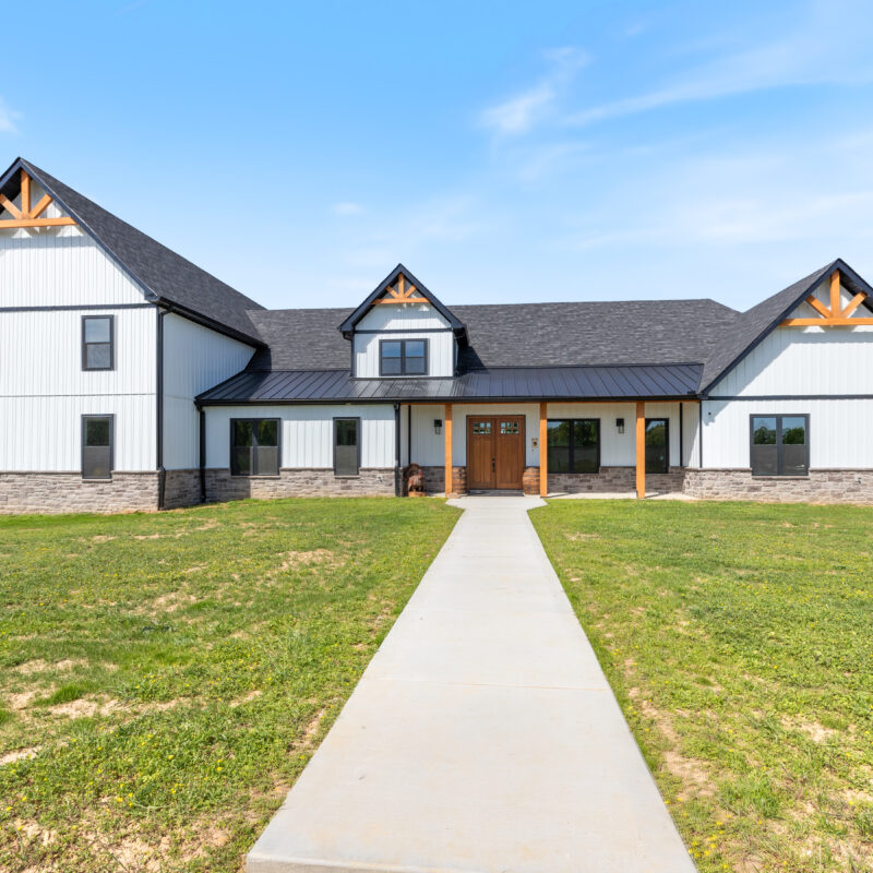 image of a large custom home with white board and batten siding and black window trim and wood accents