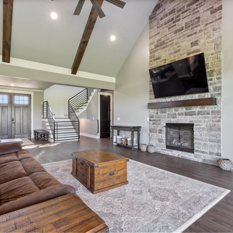 photo of an open floor plan living room with dark wood floors, custom stone fireplace wall, and wooden beams on ceiling