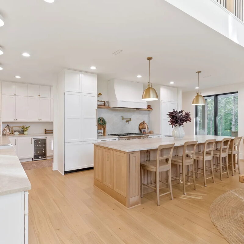 image of a wide open kitchen with white cabinets, light colored quartz countertops, large island, and gold fixtures