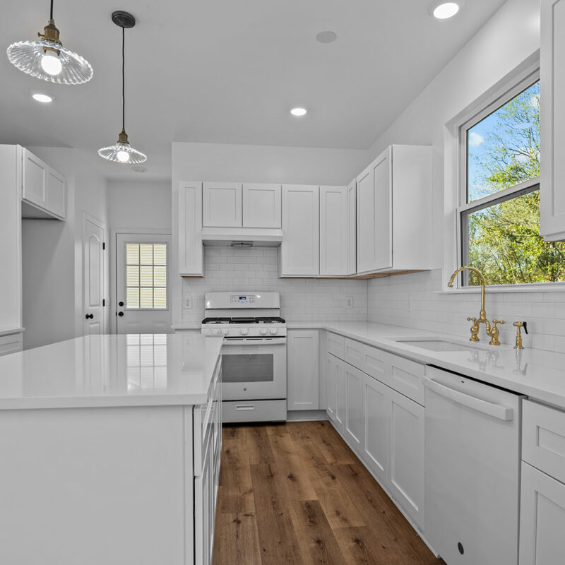 photo of a kitchen with white cabinets, white counter tops, white subway tile, and gold fixtures