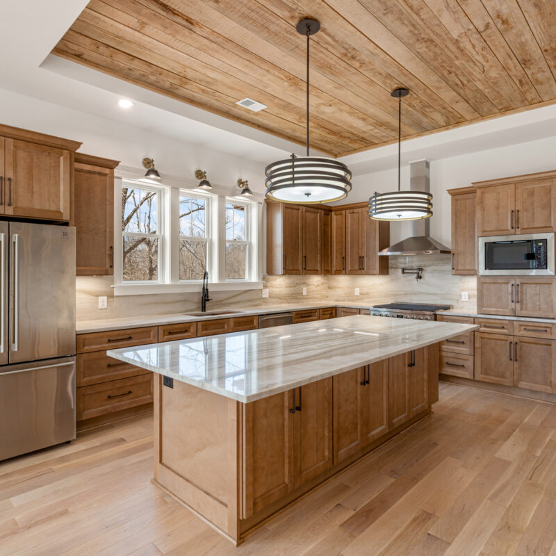 photo of a kitchen with wooden cabinetry, granite counter tops and backsplash, large island, and wood inlay on ceiling