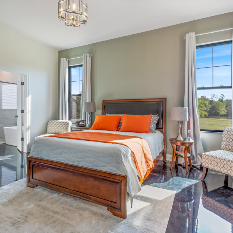 photo of a bedroom with large windows, stained marbled concrete floor, looking into bathroom with custom tile shower and freestanding tub