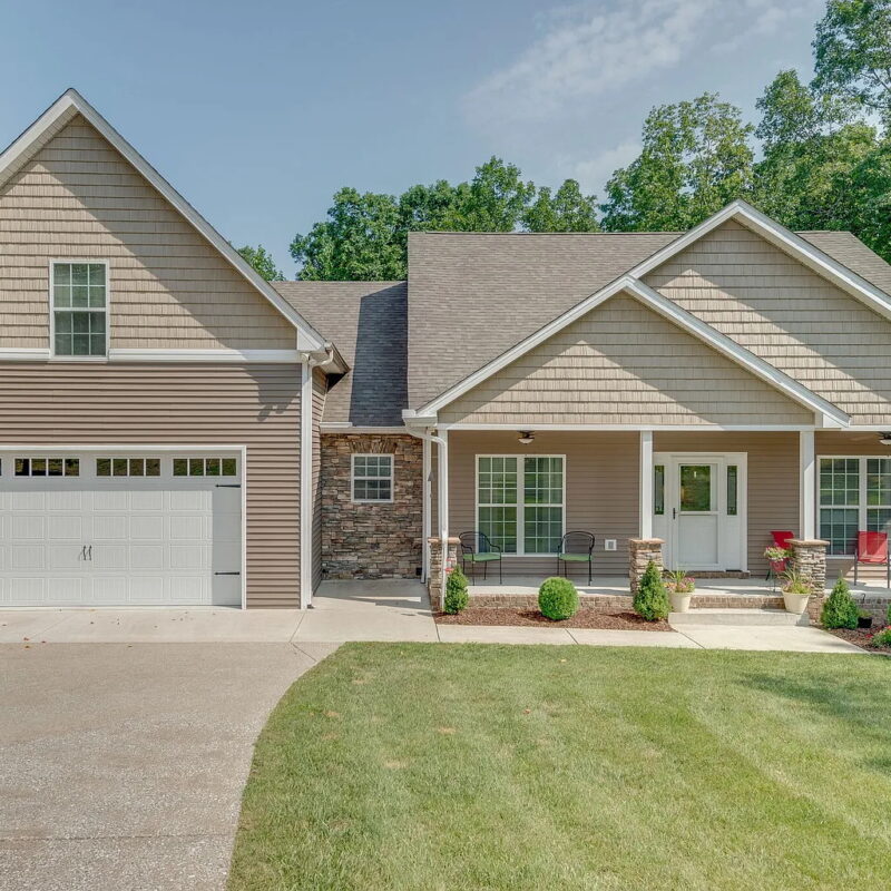 photo of a home exterior with tan siding, brick details, landscaping, and large front yard, and attached garage
